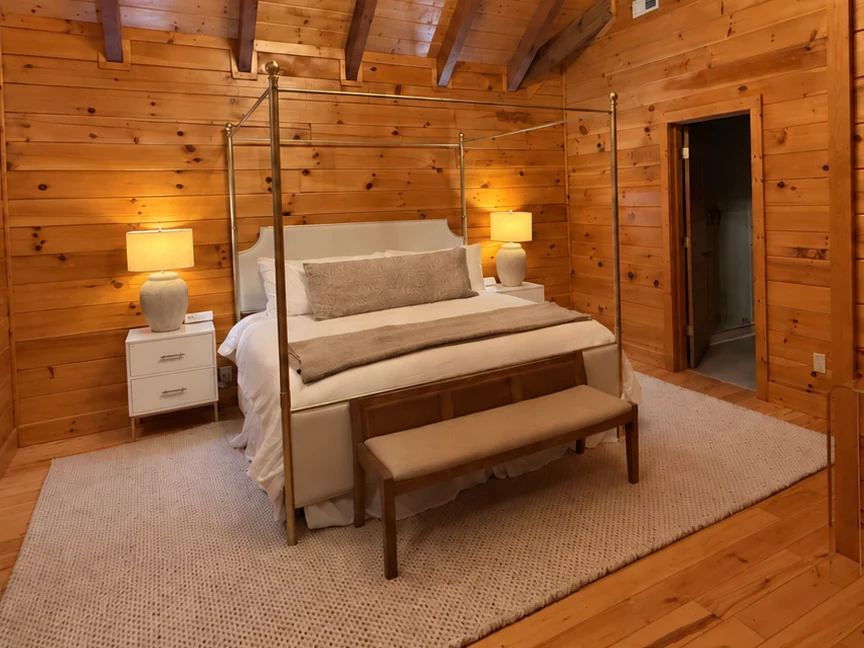 Brass four-poster king bed with cream bedding, a woven bench and paired bedside lamps in a timber-lined bedroom.