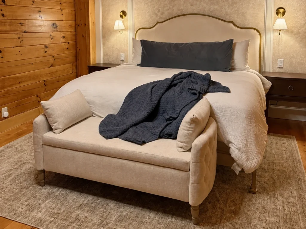 Cream upholstered king bed with a dark knitted throw and matching padded bench against a patterned headboard wall.