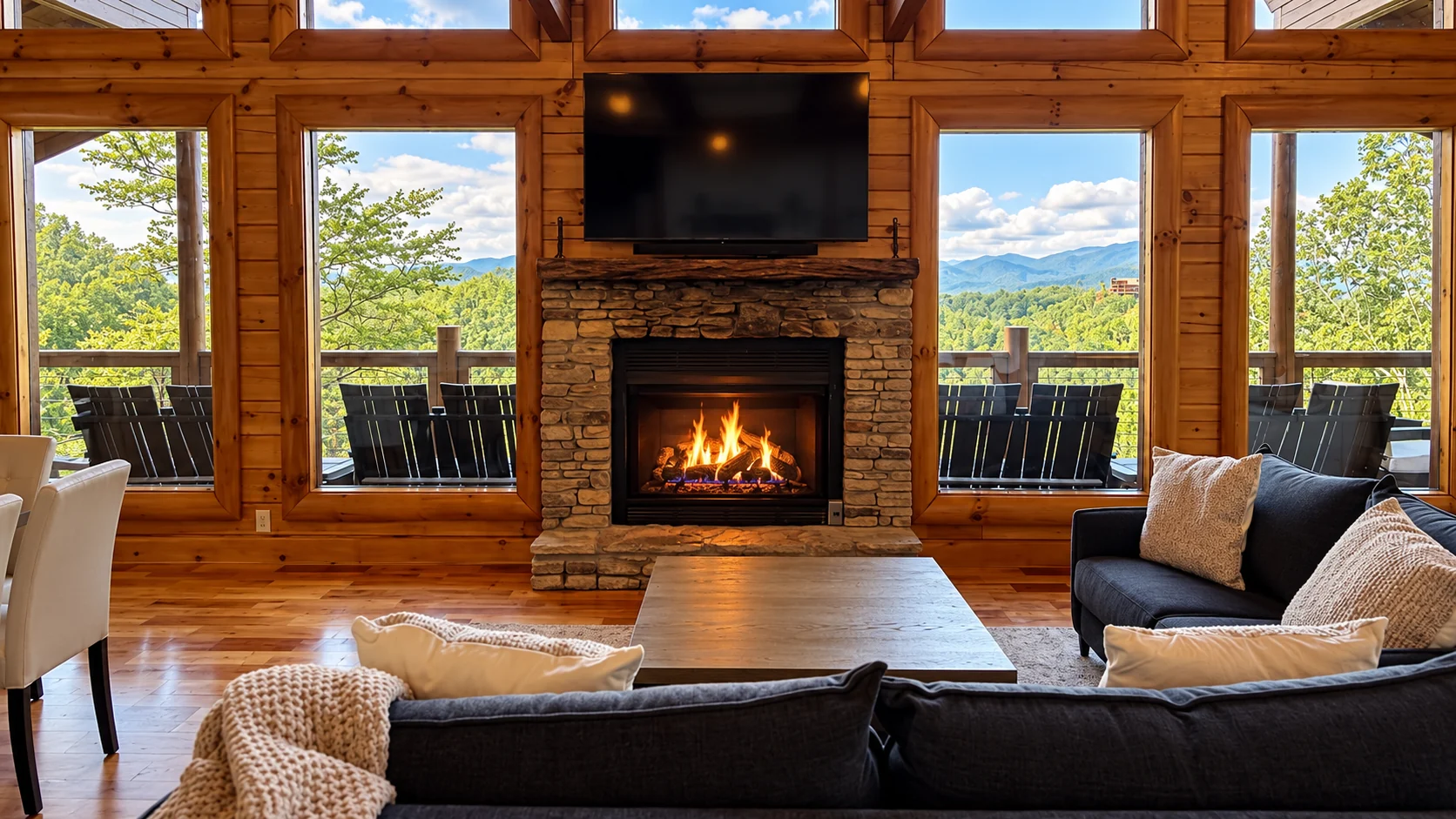 A lit stone fireplace between mountain-view windows in Engle Haven’s timber-lined great room.