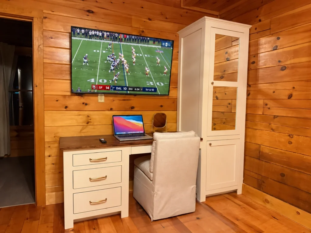 A dedicated desk workspace beneath a television showing live sports.