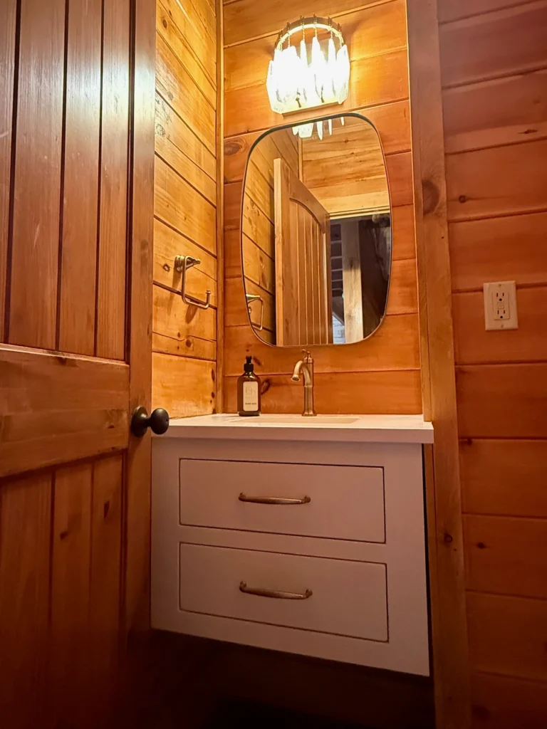 A compact vanity and oval mirror in the timber-lined half bath.