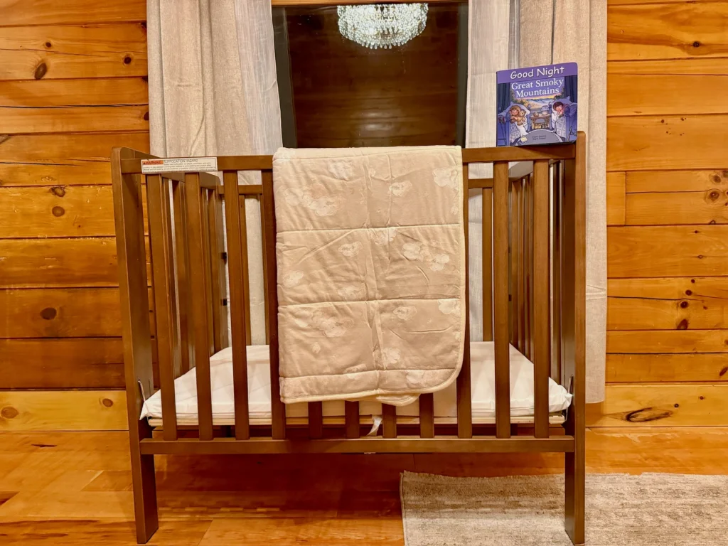 A wooden crib with a cream quilt beside the bedroom window.