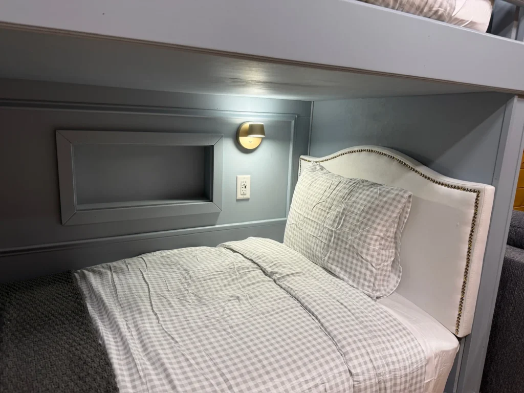 Checked bedding, an individual light and a recessed bedside cubby in a lower bunk.