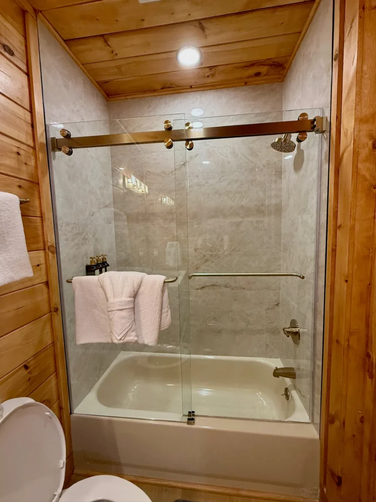 A bathtub with a glass shower enclosure and towels close by.
