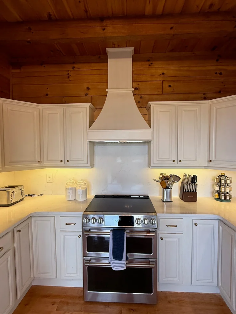 A stainless-steel range beneath the hood, surrounded by white cabinets.
