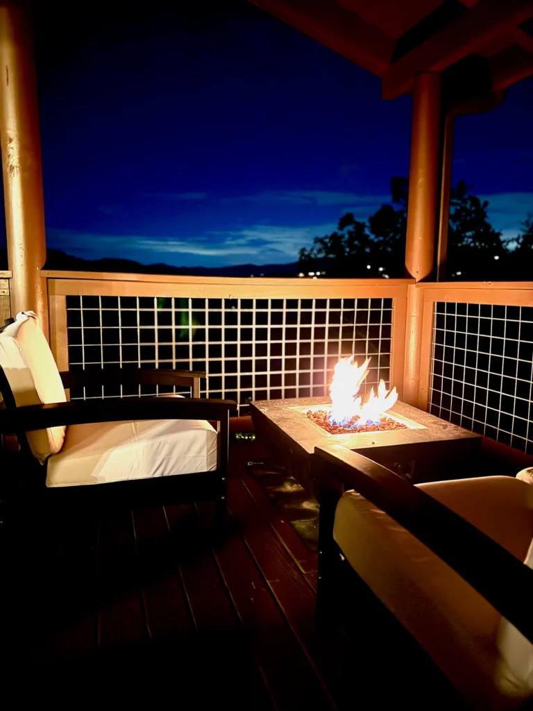 A lit fire table and cushioned seating beneath the evening mountain sky.