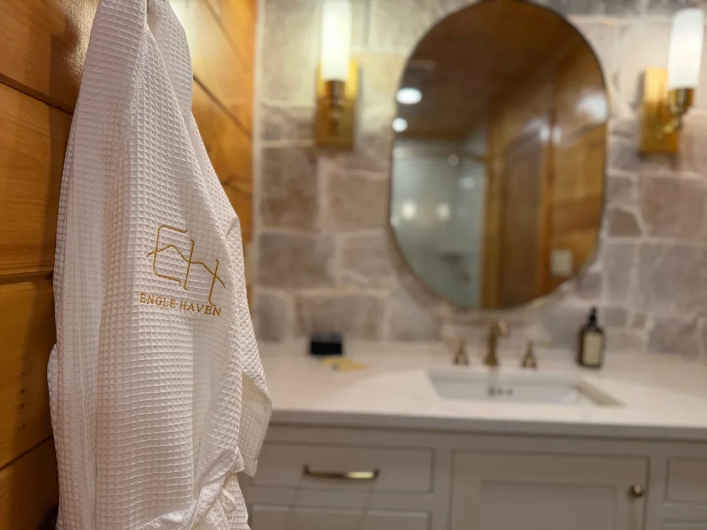An embroidered Engle Haven robe hangs beside the softly lit bathroom vanity.