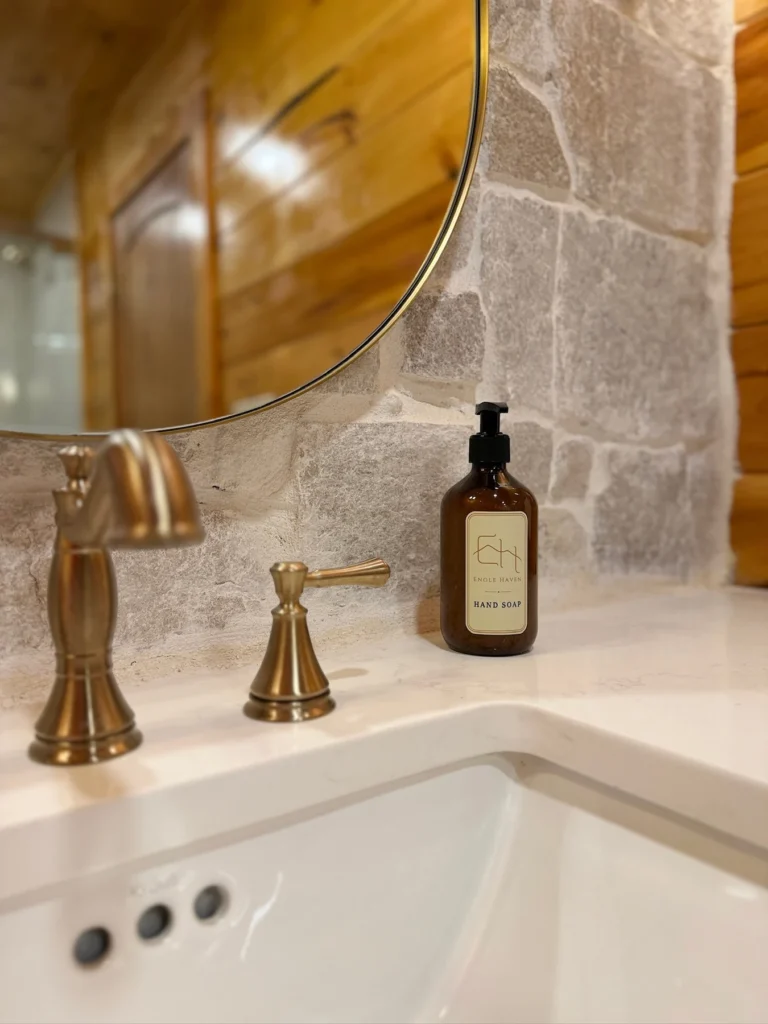 A white sink and brass faucet beneath the bathroom’s oval mirror.