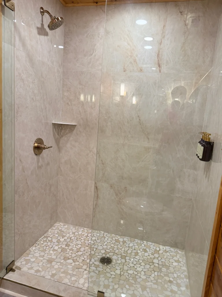 Large tile walls, a pebble-style floor and a corner shelf inside the shower.