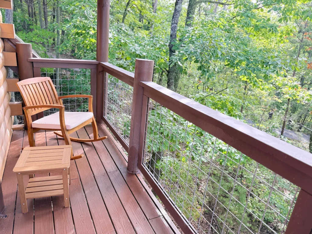 Two wooden rocking chairs on the upper deck, surrounded by trees.