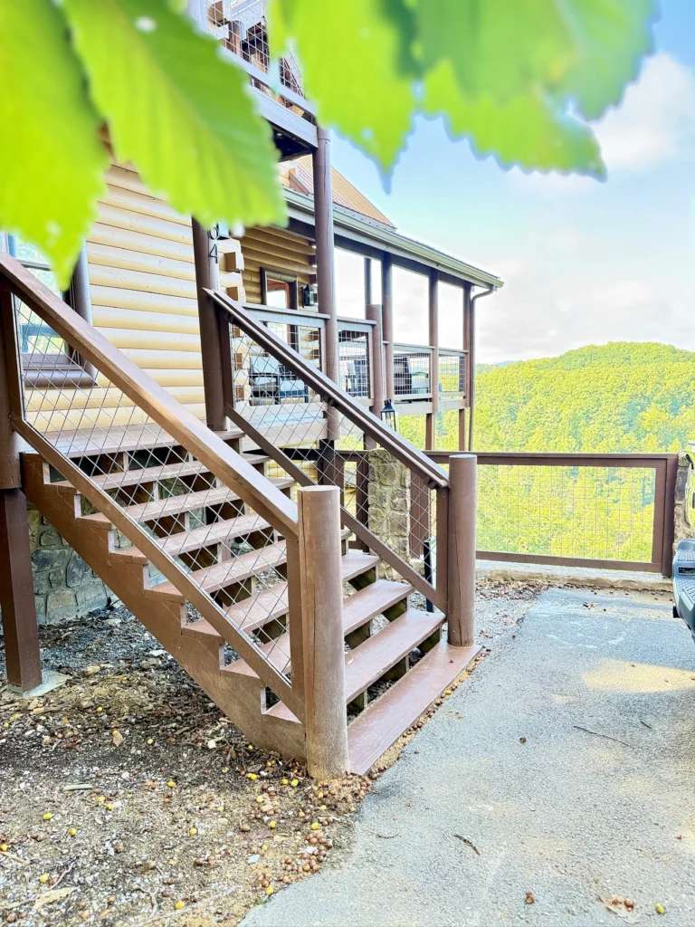 Timber stairs connect the cabin’s covered decks beside the driveway.