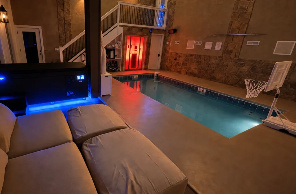 Indoor pool beside the red-lit sauna, cold plunge and cushioned seating.