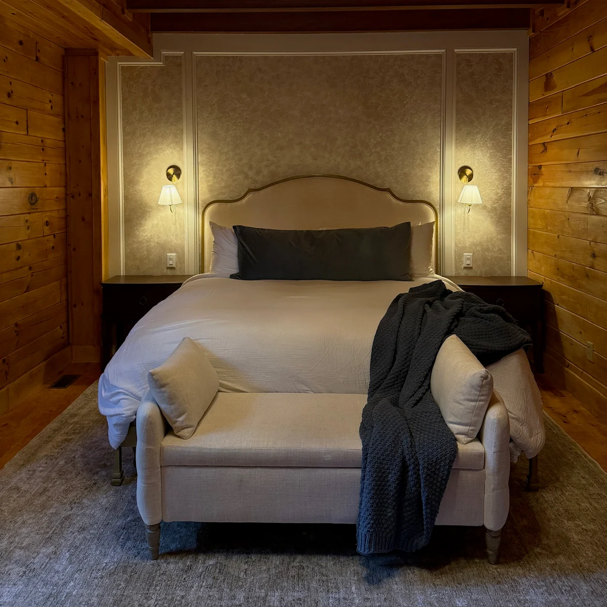 A warmly lit bedroom with a cream bed, light linens and an upholstered loveseat at its foot.