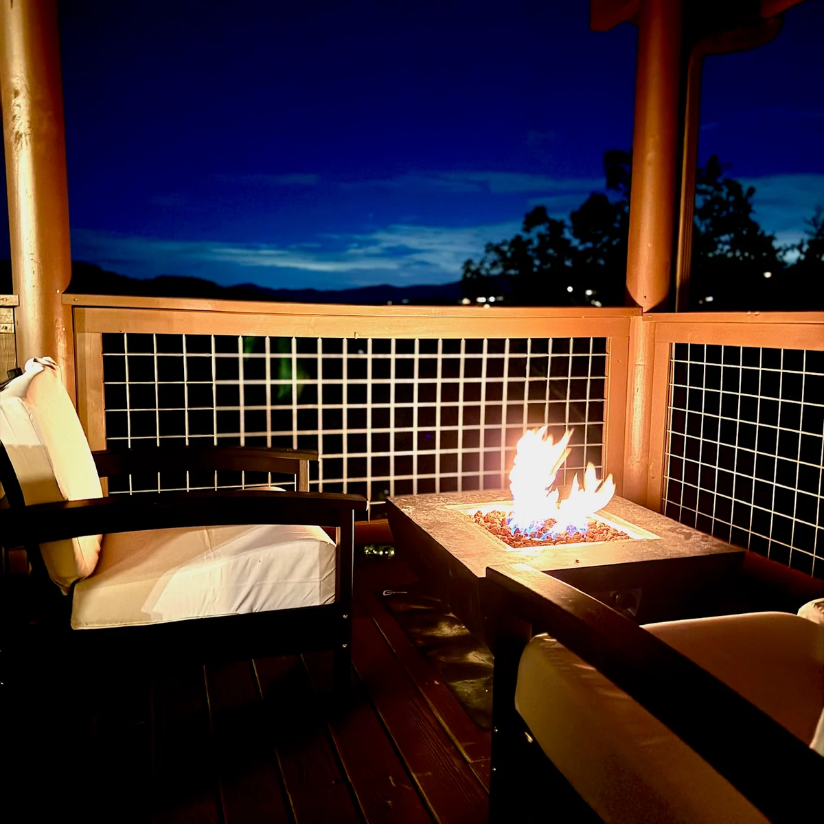 Cushioned deck seating beside a glowing fire table, with the mountain skyline at dusk.