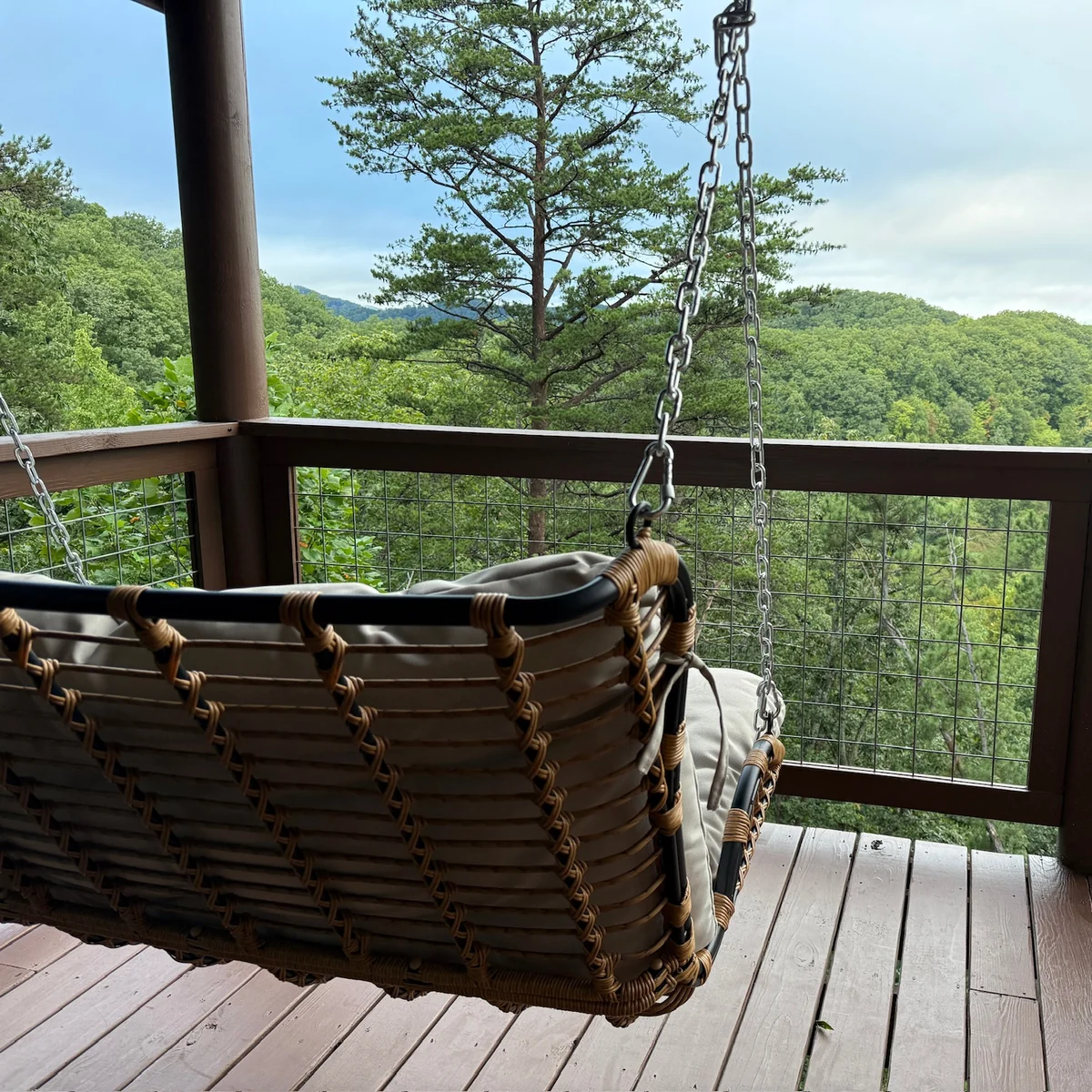 A woven hanging loveseat on the covered deck overlooking wooded hills.