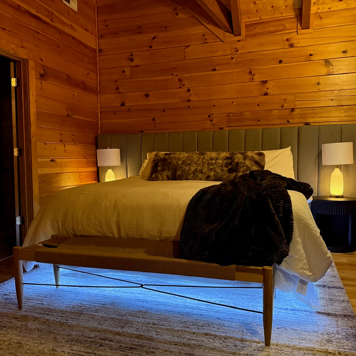 A wood-paneled bedroom with warm bedside lamps and blue lighting beneath the bed.
