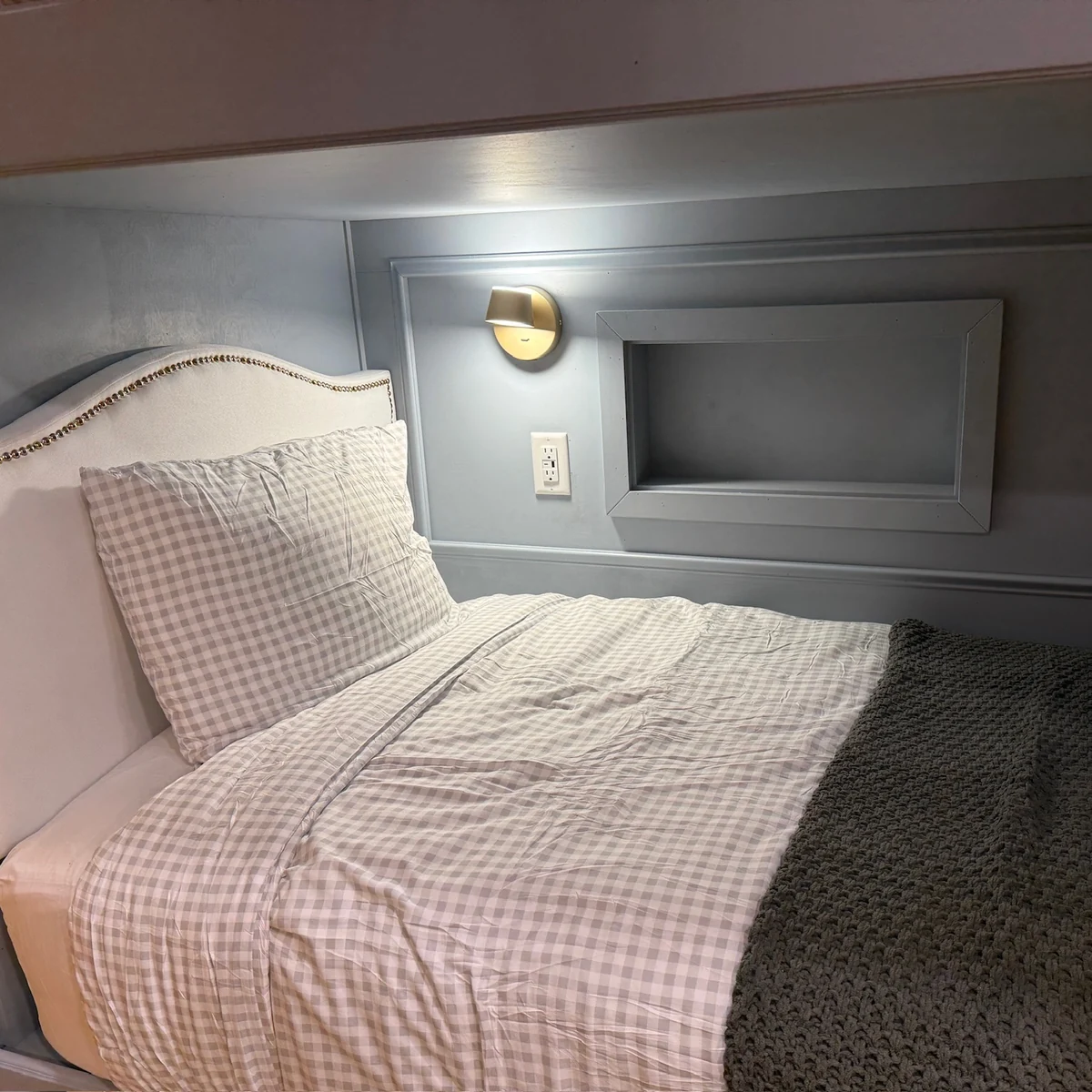 A bunk bedside with a reading light, power outlet and recessed storage cubby.