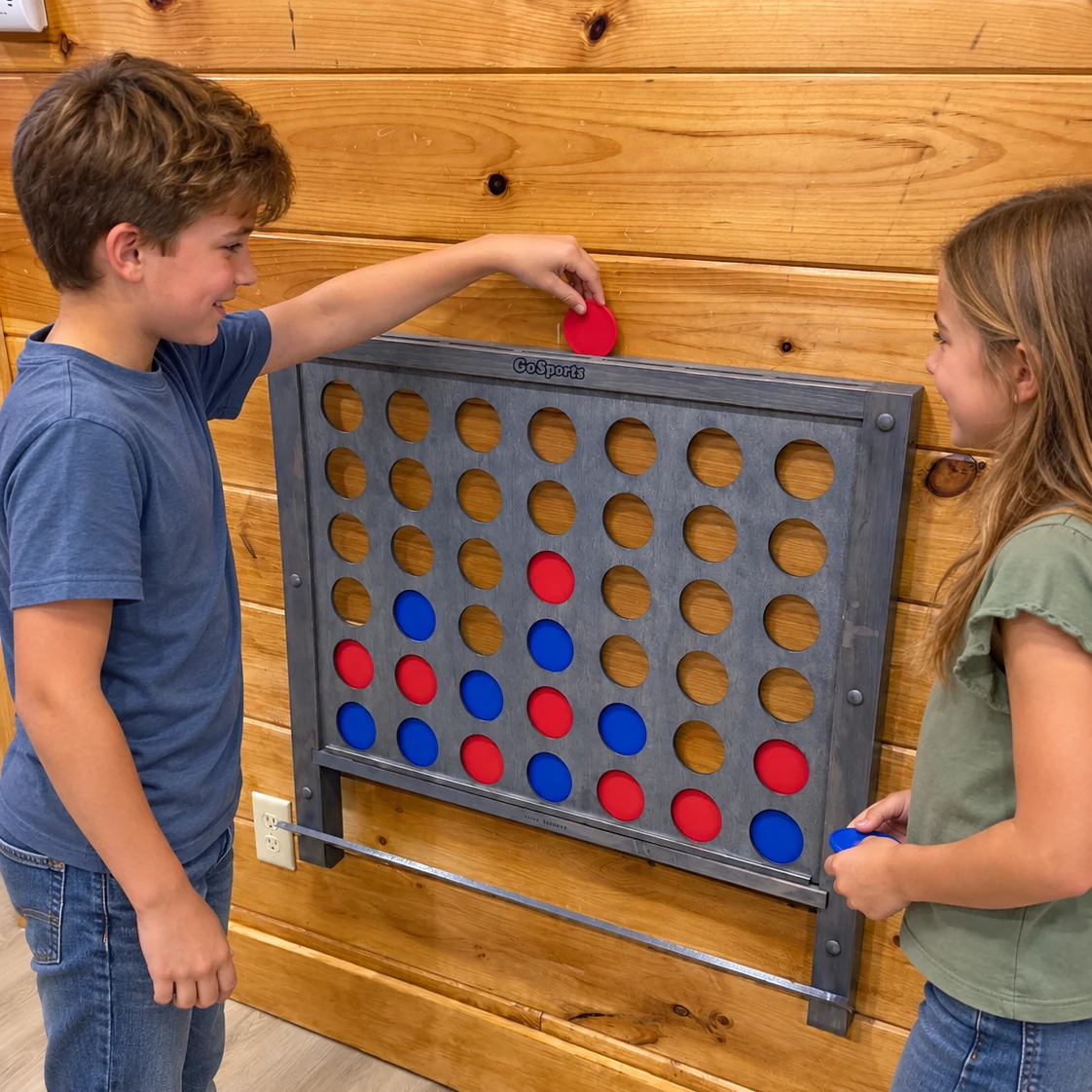 Two players placing red and blue discs in the wall-mounted Connect Four board.