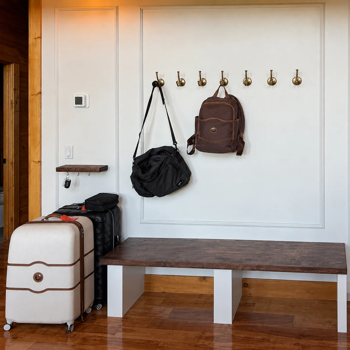 Bags on entry hooks above a storage bench, with luggage alongside.