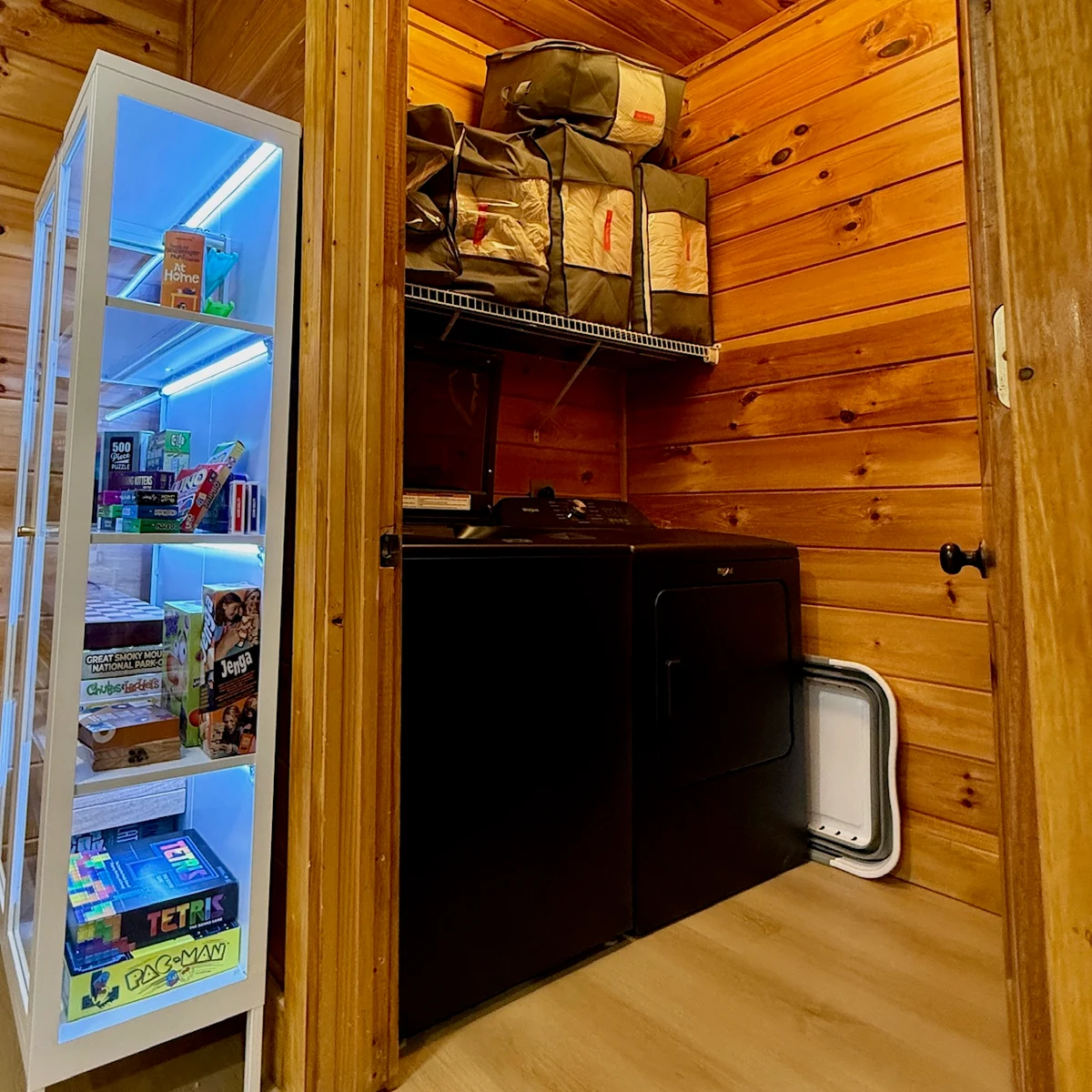 Laundry appliances in a wood-paneled utility nook beside a game cabinet.