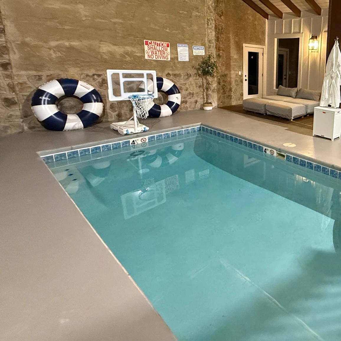 Indoor pool beside striped floating rings and a poolside basketball hoop.