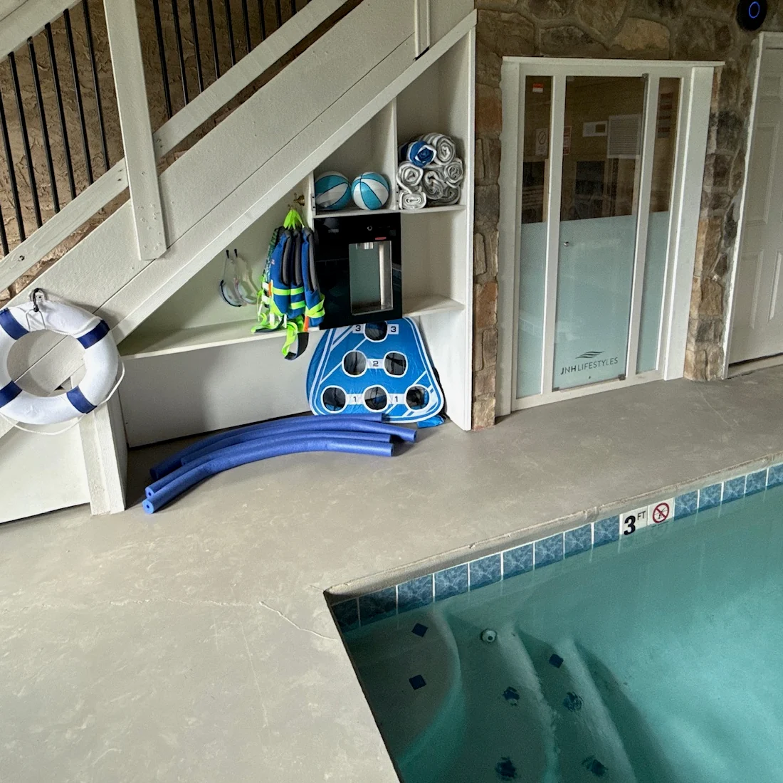 Life jackets, pool equipment and a floating cornhole board stored beside the indoor pool.