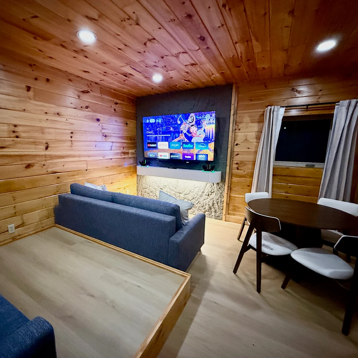 Blue seating facing a wall-mounted television in the wood-paneled entertainment room.