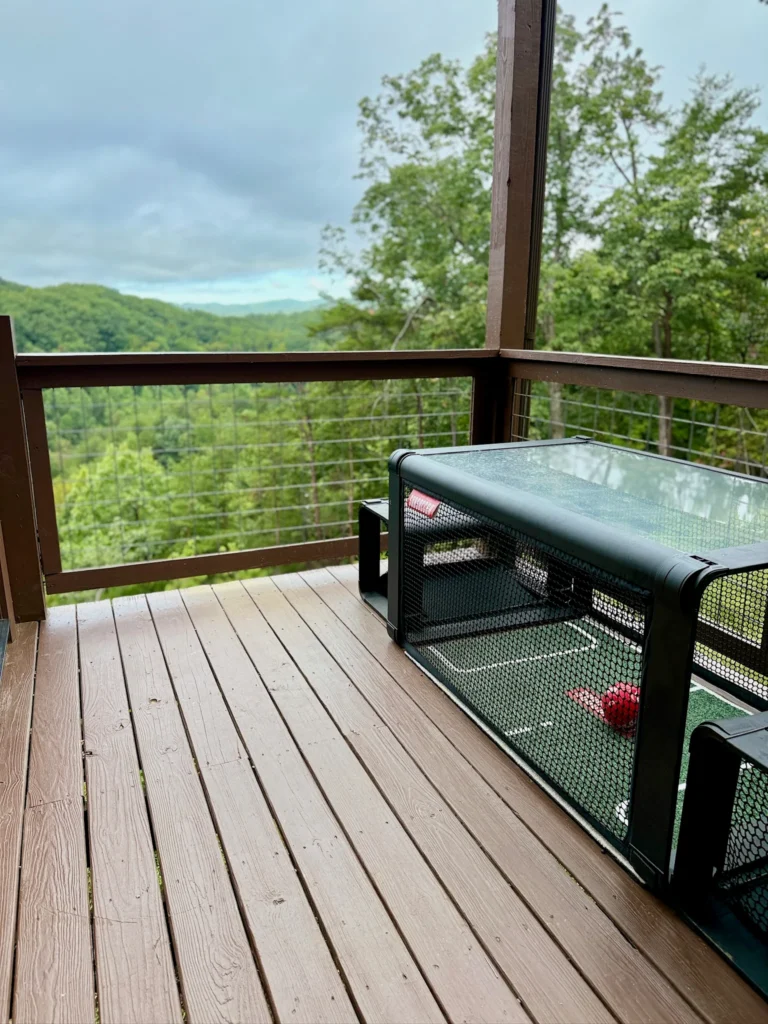 Subsoccer table with enclosed netting and a red ball on the covered deck overlooking wooded mountains.