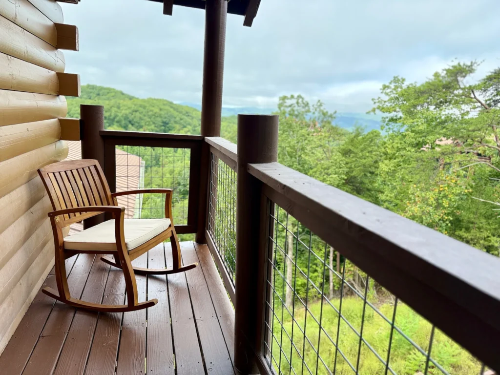 Wood rocking chair on a narrow upper deck with trees and distant mountains.
