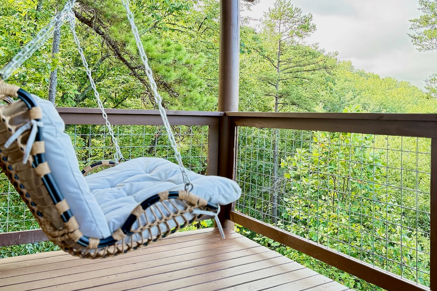 White-cushioned hanging chair on a covered timber deck overlooking green woodland.