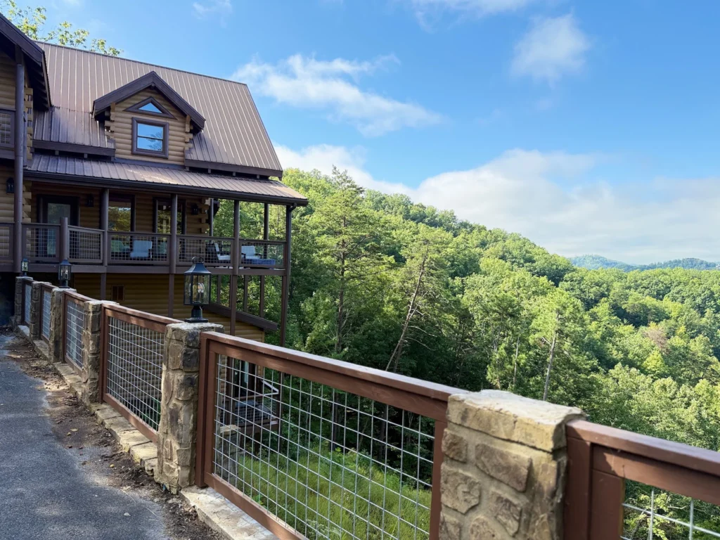 Cabin exterior and paved approach beside stone posts and a railing overlooking the hills.