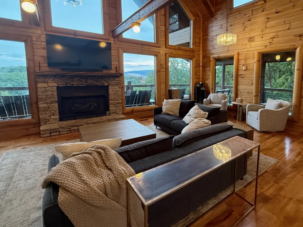 Stone fireplace, sofas and tall windows overlooking the wooded hills in the great room.