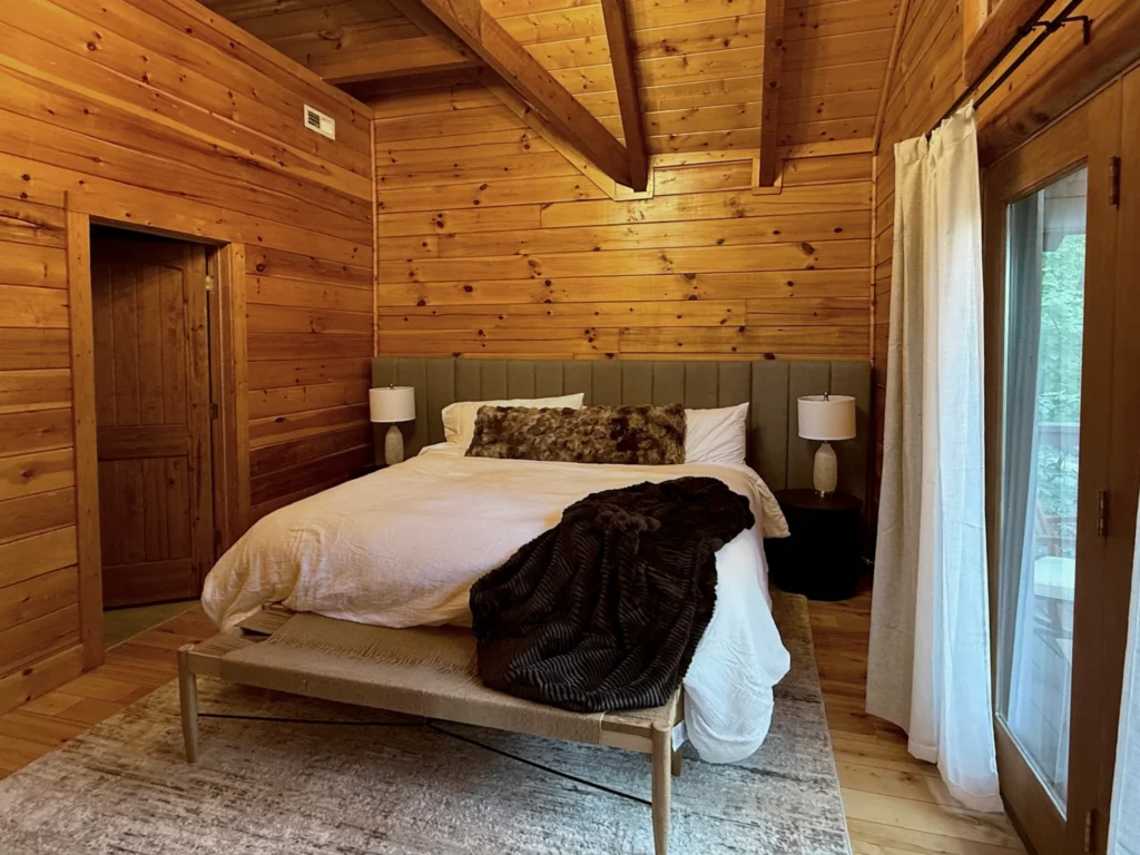King bed with an olive upholstered headboard, pale bedding and glazed doors to the deck.