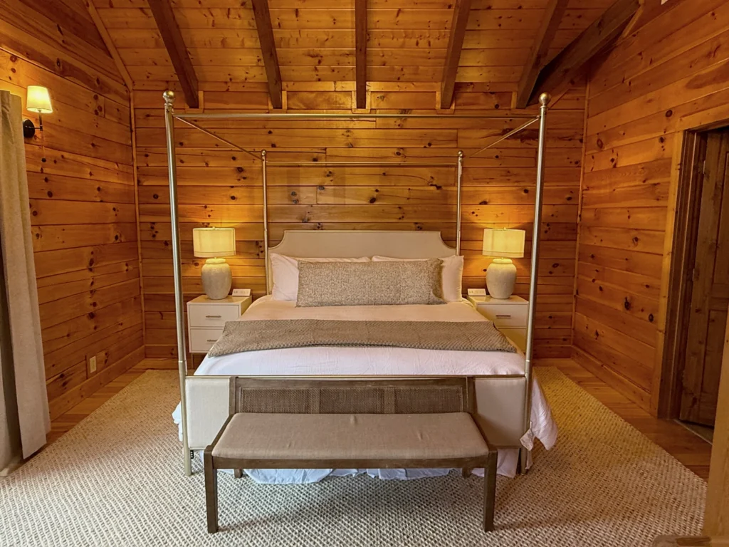Four-poster king bed with a foot-of-bed bench and paired lamps in a timber-lined bedroom.