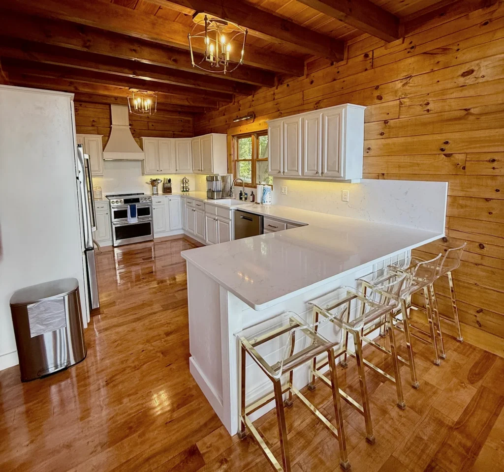 White kitchen cabinets, stainless appliances and breakfast-bar seating beneath a wood ceiling.