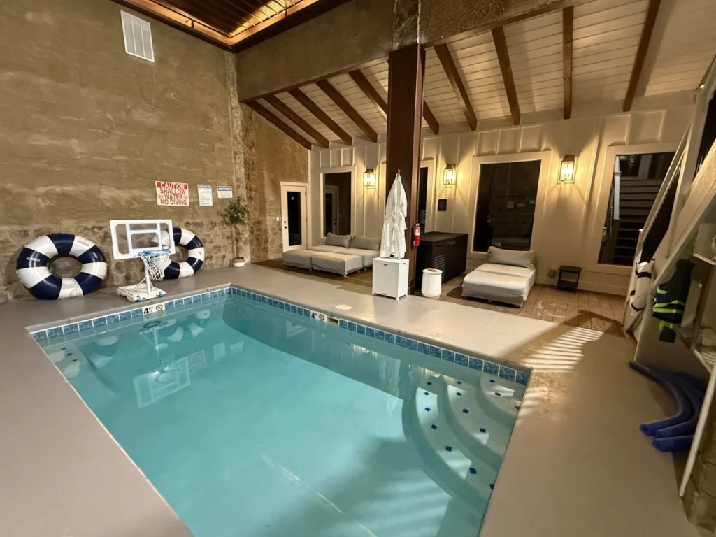 Indoor pool with submerged steps, stone walls and cushioned loungers; safety signs and pool equipment remain visible.