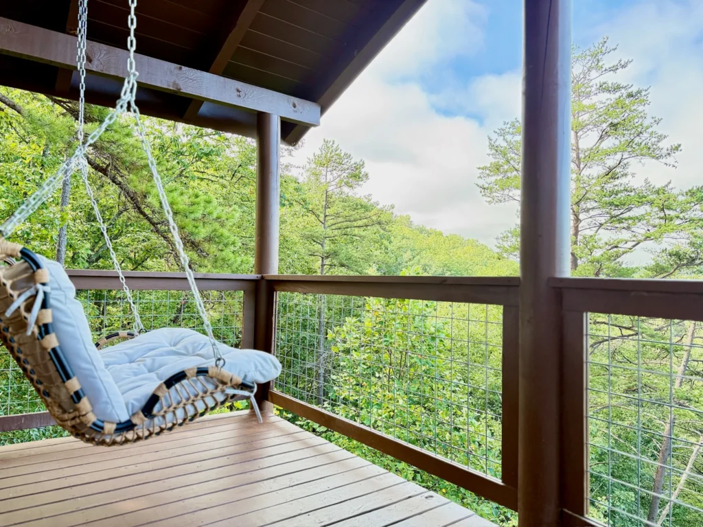 Cushioned hanging chair on a covered deck overlooking the wooded hills.